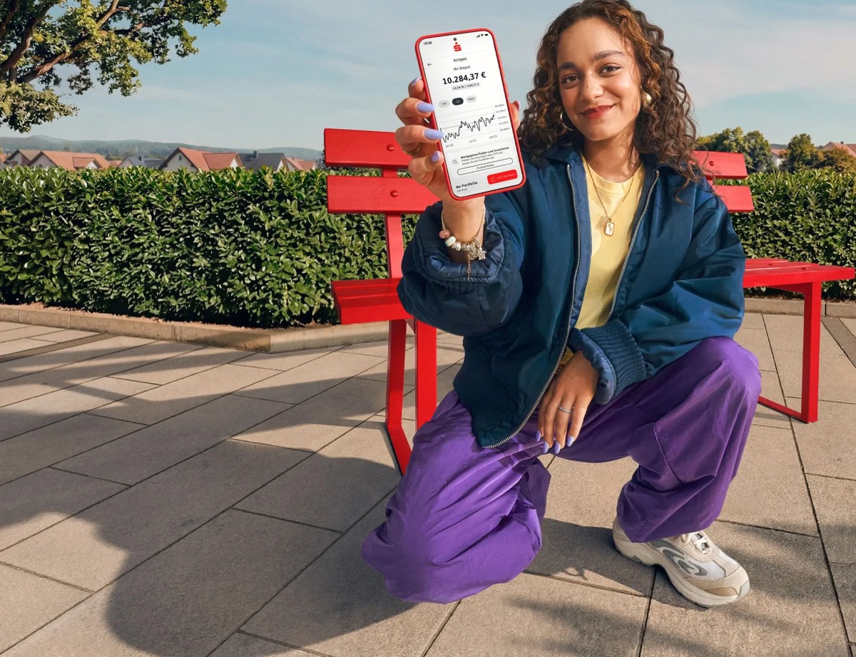 Junge Frau auf einer roten Bank zeigt ihr S-Neo Depot in der App Sparkasse